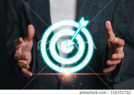 A businessman in a suit holding a glowing virtual target board with an arrow, representing success, precision, and goal achievement in a modern business context. 116351782