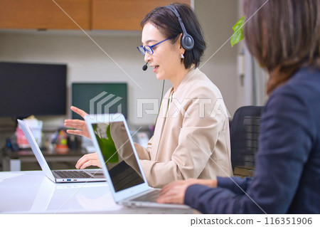 A middle-aged woman working in an office wearing a headset 116351906