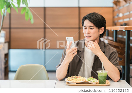 A young Asian man using a smartphone in a cafe or at home (troubled, worried, thinking, trouble, failure, shock) A young Asian man using a smartphone in a cafe or at home (troubled, worried, thinking, trouble, failure, shock) 116352125