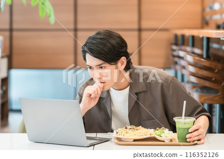 一個年輕的亞洲男子在咖啡館吃飯時看著電腦(驚訝,新聞,驚訝,發現,發現) 一個年輕的亞洲男子在咖啡館吃飯時看著電腦(驚訝,新聞,驚訝,發現,發現) 116352126