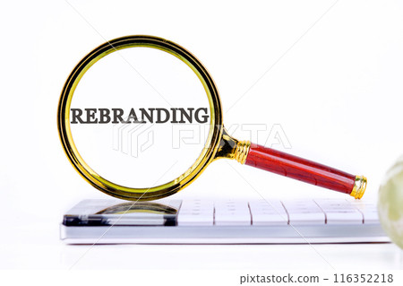 Business and rebrand concept. Copy space. REBRANDING symbol through a magnifying glass standing on a calculator on a white background Business and rebrand concept. Copy space. REBRANDING symbol through a magnifying glass standing on a calculator on a white background 116352218