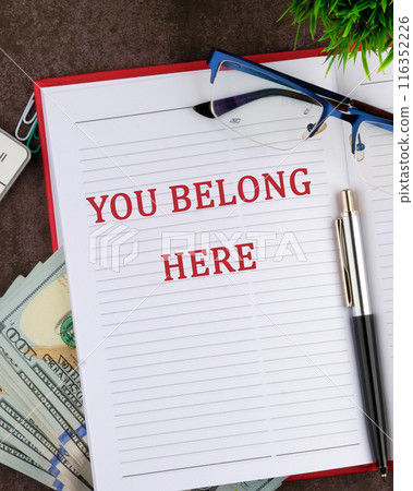 Diversity, business, inclusion and belonging concept. YOU BELONG HERE in a red business notebook in a composition with money and glasses Diversity, business, inclusion and belonging concept. YOU BELONG HERE in a red business notebook in a composition with money and glasses 116352226