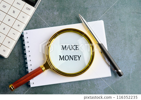 Business and Make Money concept. Copy space. Make Money symbol through a magnifying glass in a notebook on a gray background 116352235