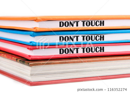 Words DO NOT TOUCH written on the ends of notebooks lying on top of each other on a white background Words DO NOT TOUCH written on the ends of notebooks lying on top of each other on a white background 116352274