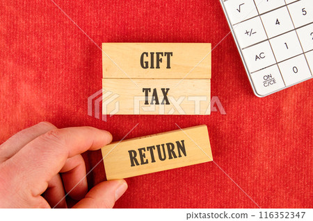 Text GIFT TAX RETURN on wooden blocks with a hand, part of a calculator on a red background Text GIFT TAX RETURN on wooden blocks with a hand, part of a calculator on a red background 116352347