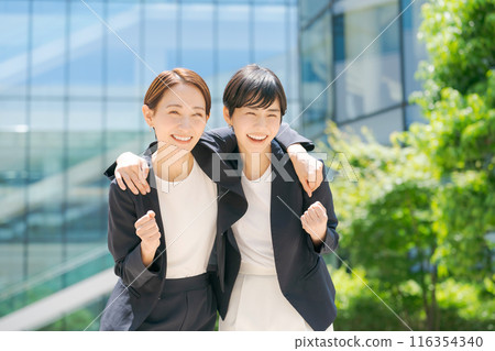 Women in suits laughing with their arms around each other Women in suits laughing with their arms around each other 116354340