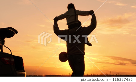 Silhouettes of family playing running at sunset near car, automobile. Man and woman running in circle, girl sitting on father's shoulders. Genuine joy, boundless fun in nature at setting evening sun. Silhouettes of family playing running at sunset near car, automobile. Man and woman running in circle, girl sitting on father's shoulders. Genuine joy, boundless fun in nature at setting evening sun. 116357485