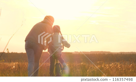 Woman teaching girl to ride bike, silhouettes at sunrise. Exciting activities with family, older, mom and daughter spend time together. Playful interesting form of learning to ride bike. Fun childhood Woman teaching girl to ride bike, silhouettes at sunrise. Exciting activities with family, older, mom and daughter spend time together. Playful interesting form of learning to ride bike. Fun childhood 116357498