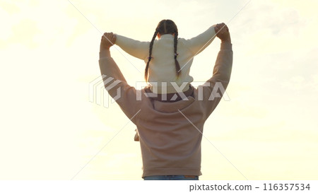 Girl on father shoulders walking forward. Man and child walking towards bright white sunlight. Loving dad and beloved daughter. Concept of fatherhood, parenthood, strong support, prop for little kid. Girl on father shoulders walking forward. Man and child walking towards bright white sunlight. Loving dad and beloved daughter. Concept of fatherhood, parenthood, strong support, prop for little kid. 116357534