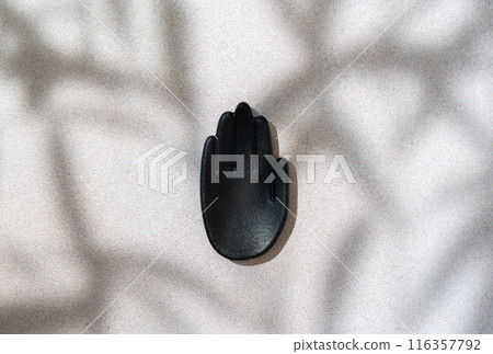 Beauty or cosmetic product presentation scene made with mockup black hand-shaped sculpture on textured surface with defocused leaves shadow. Studio photography. 116357792
