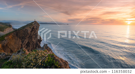 A woman looks out to sea from a cliff at sunset. A woman looks out to sea from a cliff at sunset. 116358032