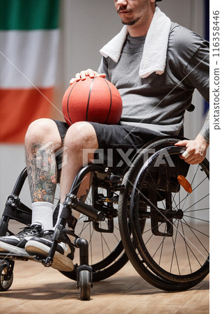 Vertical cropped shot of tattooed sportsman with disability using wheelchair and holding ball during basketball practice with dramatic light 116358446