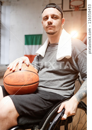 Vertical portrait of man with disability using wheelchair in indoor basketball court with dramatic light Vertical portrait of man with disability using wheelchair in indoor basketball court with dramatic light 116358453