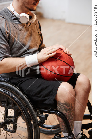 Vertical cropped shot of young sportsman using wheelchair while playing basketball indoors and holding ball Vertical cropped shot of young sportsman using wheelchair while playing basketball indoors and holding ball 116358498