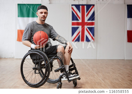 Full length portrait of young man with disability using wheelchair and looking at camera while playing adaptive basketball in indoor court copy space 116358555