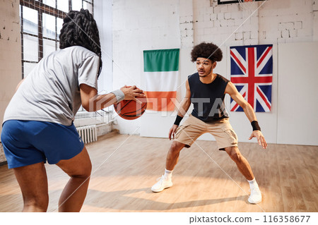 Action shot of two African American teenagers boy and girl playing basketball together at indoor court with young man standing in defense copy space 116358677