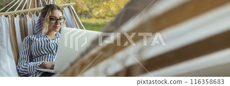 Young beautiful woman lies in a hammock with a laptop in glasses outside at home 116358683