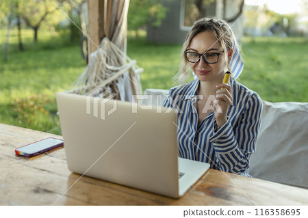 freelance girl works at a computer and smokes an electrode cigarette outside the house freelance girl works at a computer and smokes an electrode cigarette outside the house 116358695