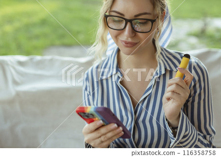 Beautiful woman smoking e-cigarette on the street and use smartphone Beautiful woman smoking e-cigarette on the street and use smartphone 116358758