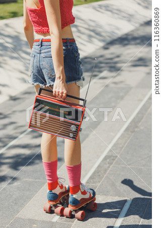 Cropped photo of skater girl, dressed in vibrant summer attire, holds retro radio and listening music, while roller skating in park. Cropped photo of skater girl, dressed in vibrant summer attire, holds retro radio and listening music, while roller skating in park. 116360869