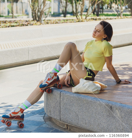 Vibrant young woman relaxing on ramp in park. Roller skater girl taking break between training session on sunny day. 116360894