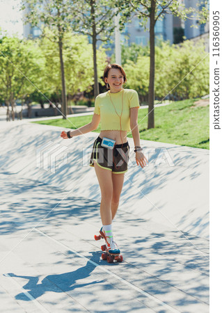 Skater girl training, rolling through park on sunny day, wearing sportswear and retro roller skates, and listening music on vintage player. 116360905
