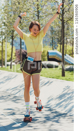 Skater girl training through city streets, wearing yellow crop top and brown shorts, and listening music on retro player. 116360906