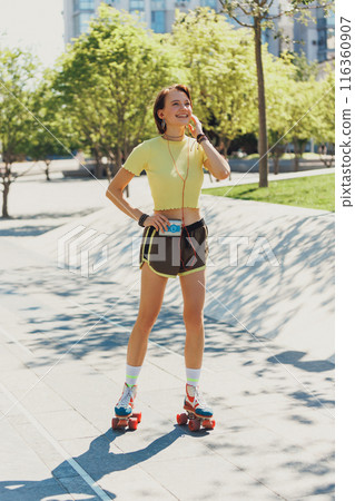 Skater girl gleefully rolling through city streets, wearing yellow crop top and brown shorts, and listening music on retro player. Skater girl gleefully rolling through city streets, wearing yellow crop top and brown shorts, and listening music on retro player. 116360907