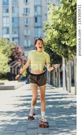 Cheerful skater girl, teenager, enjoying sunny day in city, wearing bright athletic wear and cruising on retro roller skates. 116360911