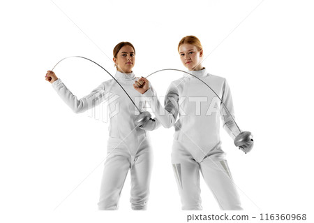 Two female fencers pose confidently with their swords, showcasing their skills and precision against white studio background. 116360968