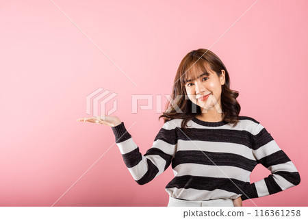 Asian happy portrait beautiful cute young woman smile standing presenting product holding something on palm away side, studio shot isolated on pink background with copy space, female show hand gesture 116361258