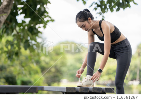 Young Woman in Athletic Wear Tying Shoelaces Outdoors in a Park Setting Young Woman in Athletic Wear Tying Shoelaces Outdoors in a Park Setting 116361267