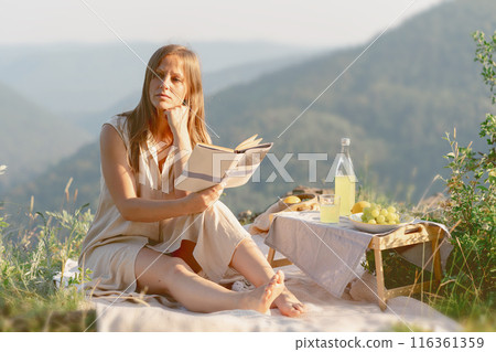 A woman is enjoying a peaceful moment reading a book during a relaxing outdoor picnic in nature A woman is enjoying a peaceful moment reading a book during a relaxing outdoor picnic in nature 116361359