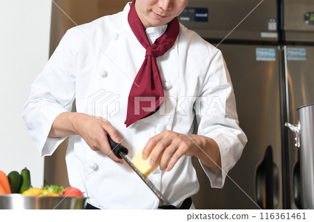 A male chef shaving cheese with a grater in the kitchen A male chef shaving cheese with a grater in the kitchen 116361461