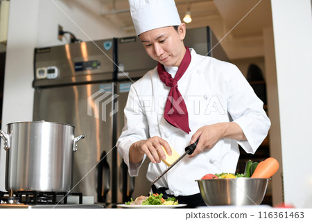 A male chef shaving cheese with a grater in the kitchen A male chef shaving cheese with a grater in the kitchen 116361463