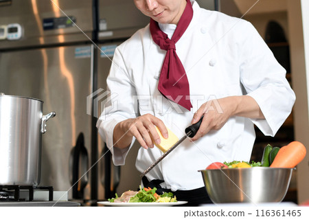 A male chef shaving cheese with a grater in the kitchen A male chef shaving cheese with a grater in the kitchen 116361465