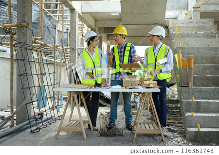 Full length of architects in safety helmets discussing a construction project at building site Full length of architects in safety helmets discussing a construction project at building site 116361743