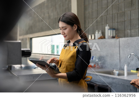 Young Barista in Yellow Apron Using Tablet in Modern Coffee Shop Young Barista in Yellow Apron Using Tablet in Modern Coffee Shop 116362956
