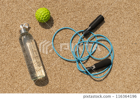 Sports set of water, jump rope and massage ball for workout and activity on outdoor sports ground. View from above. Sports set of water, jump rope and massage ball for workout and activity on outdoor sports ground. View from above. 116364196