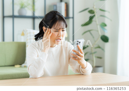 Young woman looking at her smartphone in the living room Young woman looking at her smartphone in the living room 116365253