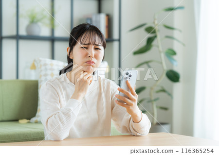 Young woman looking at her smartphone in the living room 116365254