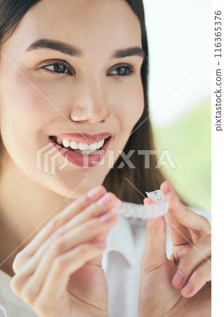 Smiling Woman Holding Aligners for Perfect Teeth 116365376