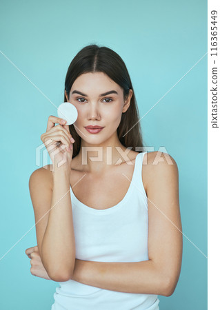 Woman Holding Cotton Pad Against Blue Background in Skincare Concept Woman Holding Cotton Pad Against Blue Background in Skincare Concept 116365449