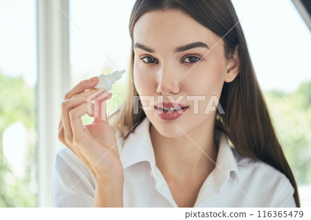 Woman Holding Eye Drops Bottle in Bright Natural Light Woman Holding Eye Drops Bottle in Bright Natural Light 116365479