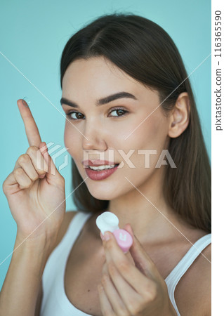 Eye Health. Woman Holding Contact Lens and Smiling Against Blue Background Eye Health. Woman Holding Contact Lens and Smiling Against Blue Background 116365590