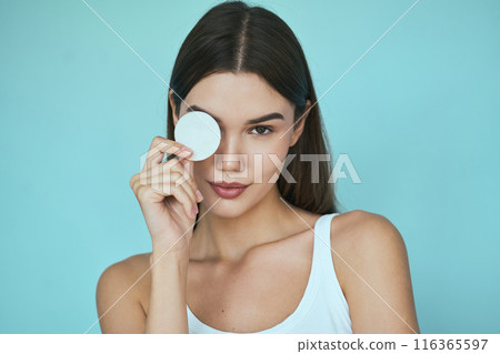 Skincare Routine. Woman Holding Cotton Pad Covering Eye on Blue Background Skincare Routine. Woman Holding Cotton Pad Covering Eye on Blue Background 116365597