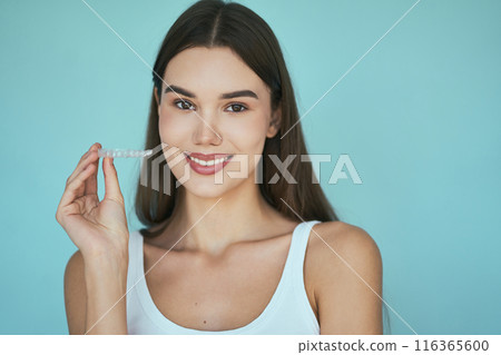 Woman Holding Clear Aligner Against Blue Background 116365600