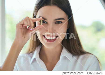 Nutrition, Health And Wellness. Smiling Woman Holding Omega-3 Near Her Eye Indoors Nutrition, Health And Wellness. Smiling Woman Holding Omega-3 Near Her Eye Indoors 116365626