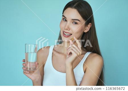 Woman Holding Vitamin Capsule And Glass Of Water On Blue Background Woman Holding Vitamin Capsule And Glass Of Water On Blue Background 116365672