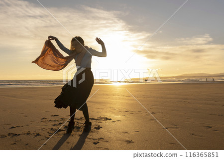 A woman is standing on a rocky hillside, with the sun setting in the background A woman is standing on a rocky hillside, with the sun setting in the background 116365851